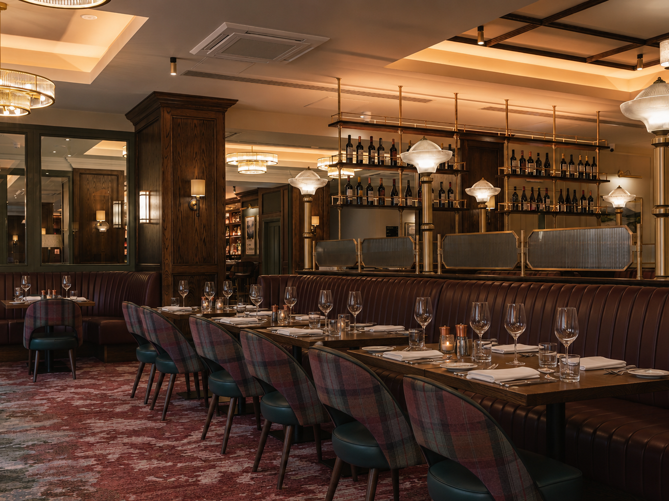 Elegant restaurant interior with dark wood accents, upholstered seating, set tables with glassware, wine bottles on shelves, and warm ambient lighting.