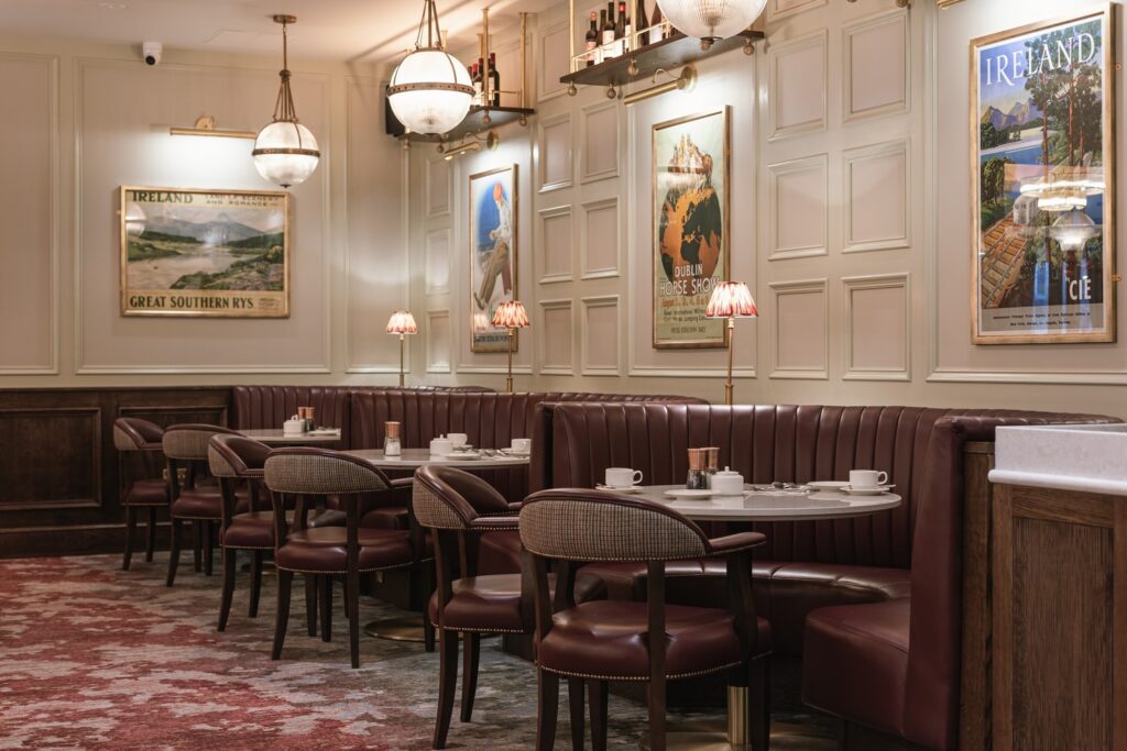 A cozy restaurant with maroon booths, round tables set with cups and saucers, wall art, vintage lamps, and paneled walls.