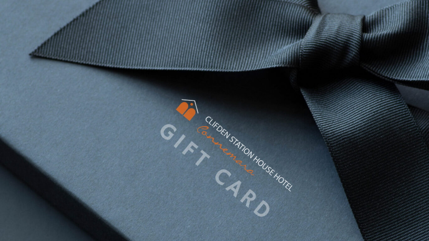 A close-up of a dark blue gift box tied with a ribbon, featuring the Clifden Station House Hotel gift card logo and text.