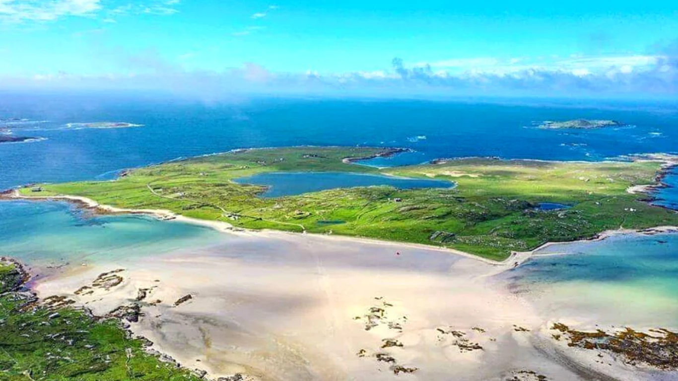 Aerial view of a sandy beach leading to a green island surrounded by blue ocean under a clear sky.