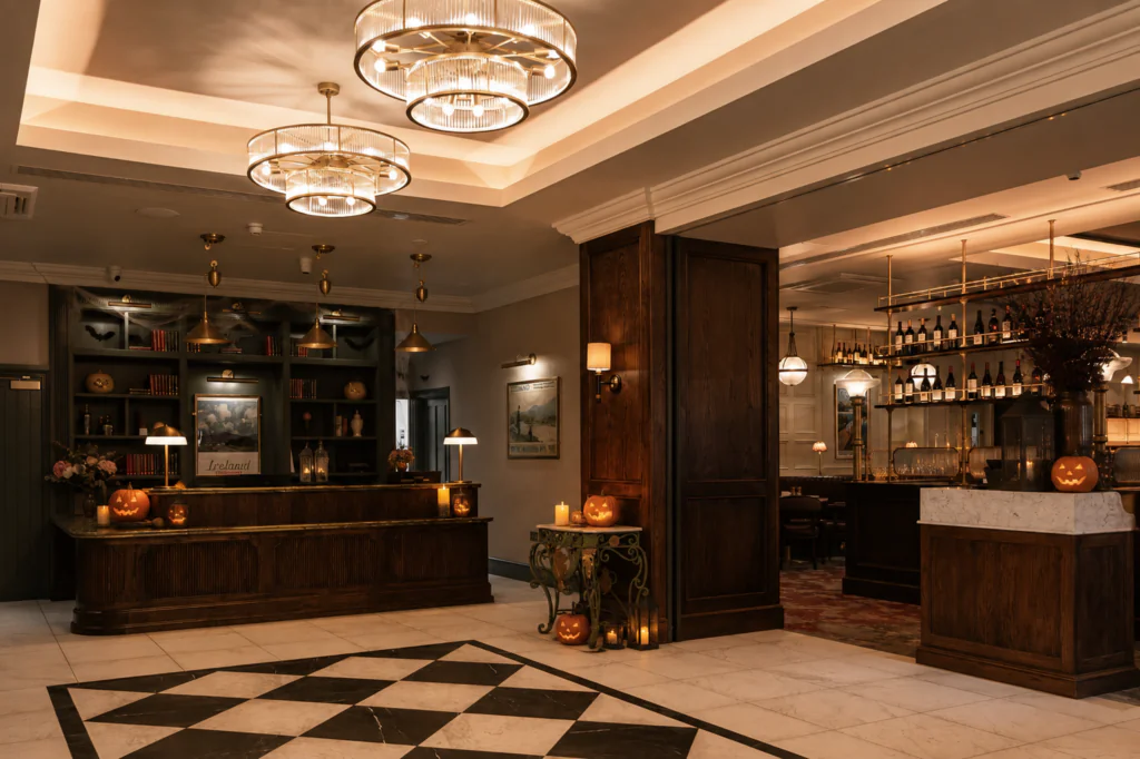 Hotel lobby with dark wood furniture, chandeliers, a checkered floor, and Halloween decorations including carved pumpkins and candles throughout the space.