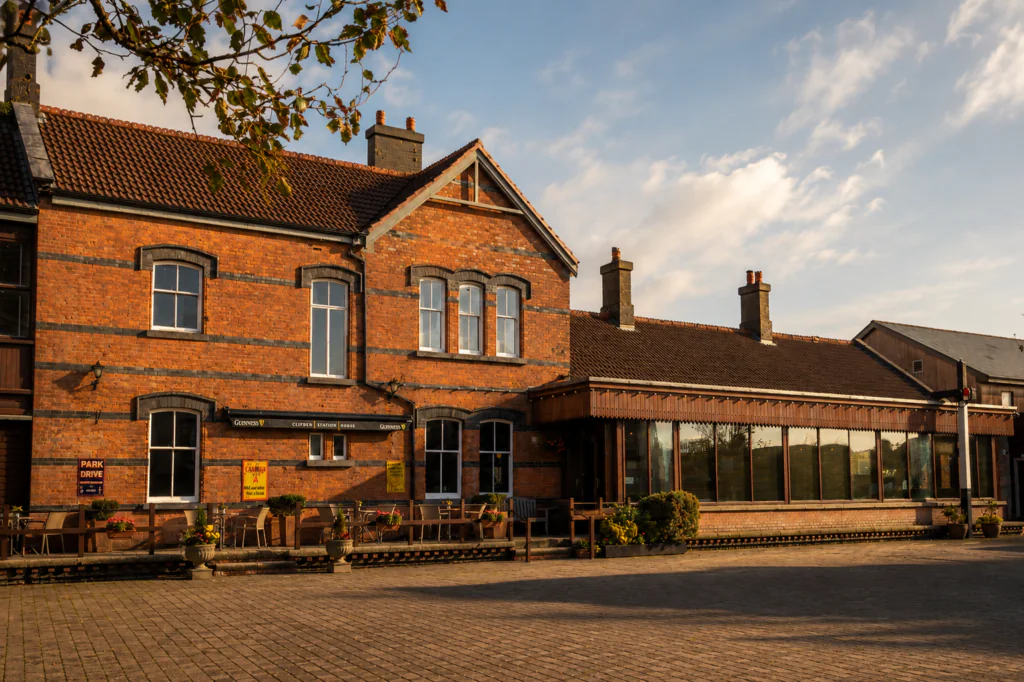 Signal Bar A brick building with large windows and a patio seating area outside, set under a partly cloudy sky in the early evening light.
