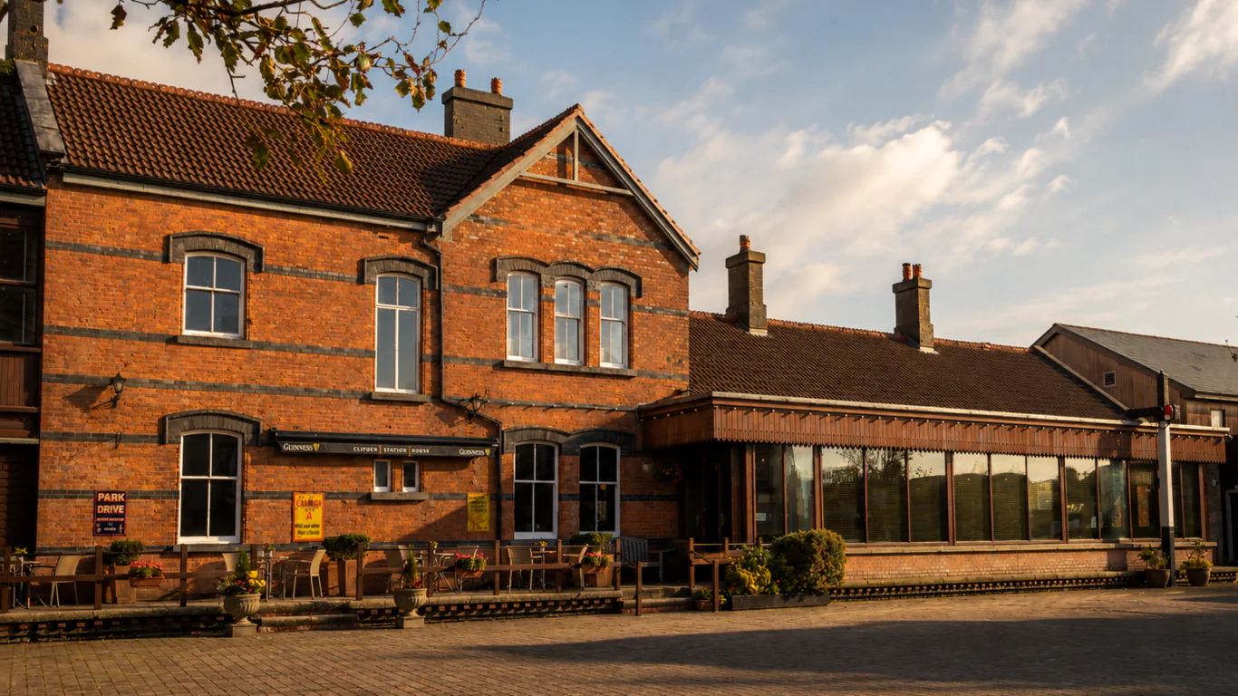 A brick building with large windows and a patio seating area outside, set under a partly cloudy sky in the early evening light.